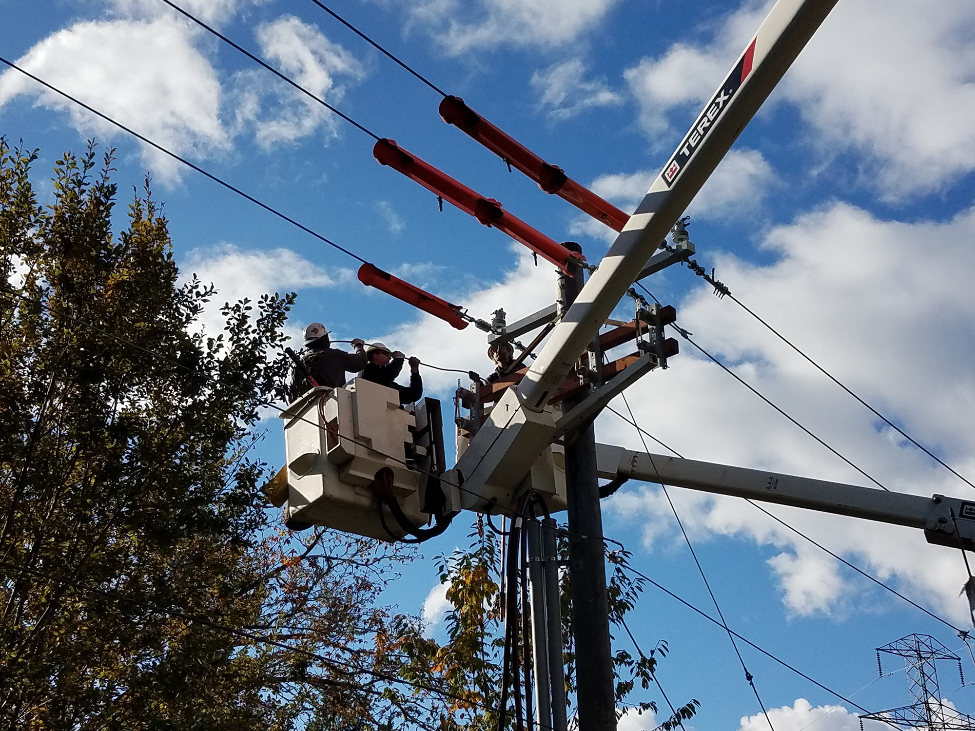 Linemen in crane bucket working on utility pole